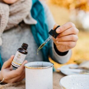 A woman adds herbal drops to a cup of tea outdoors, promoting relaxation and wellness.